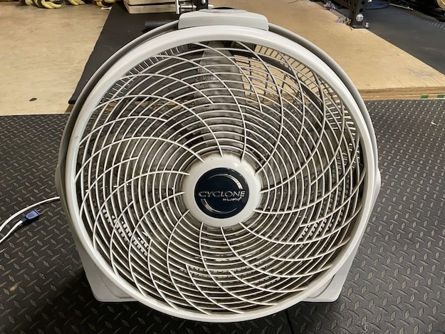 A Cyclone brand box fan with a circular grill sits on a rubber gym floor, plugged in and ready for use—perfect timing if you need tips on how to clean a box fan after an intense workout session.