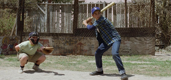 Two boys play baseball; one is batting with a bat and wearing a blue cap, while the other crouches behind him as catcher, ready to catch the ball.