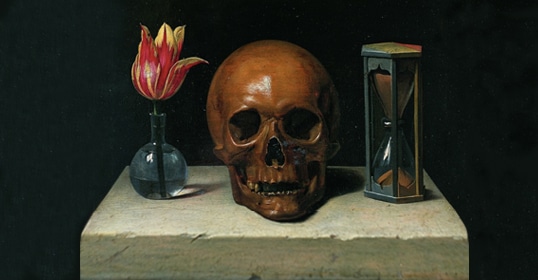 A tulip in a glass vase, a human skull, and an hourglass are arranged on a stone table against a dark background.